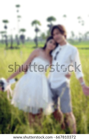 Blur style picture of wedding concept, bride with short wedding dress and bouquet of flowers in hand, hug with groom and arms open at rice field and sugar palm background.
