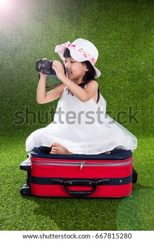Asian Little Chinese girl sitting on suitcase and playing with camera at outdoor park