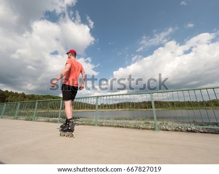 Roller skater in action. Man ride in inline skates ride along promenade handrail, blue sky in background. Low angle view