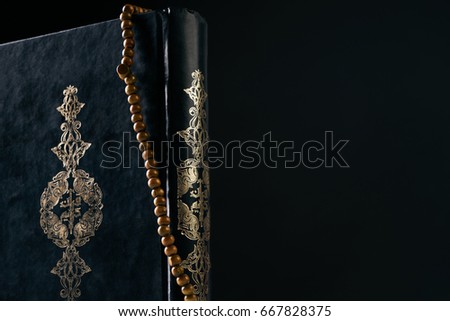 Prayer beads rosary on Koran/ Quran ( holy book of Muslims ) isolated on black background with copy space. Close-up