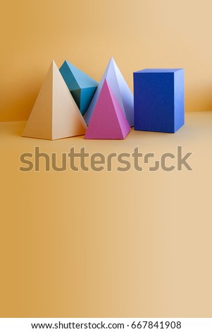 Colorful solid figures still life background. Three-dimensional prism pyramid rectangular cube objects on orange. Yellow blue pink green colored geometric shapes, soft focus photo. Copy space.
