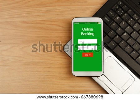 Smartphone with Online Banking on screen over laptop on wooden desk for Online Banking Payment Finance Concept, top view