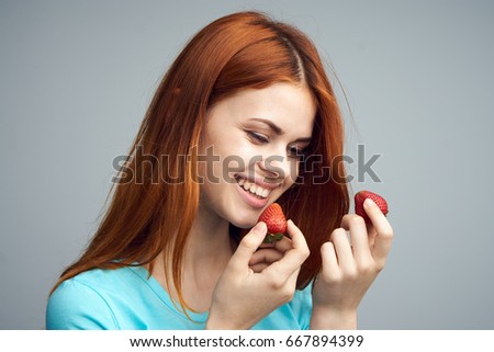 Beautiful young woman smiling and holding a strawberry on a gray background, berries, summer, joy.