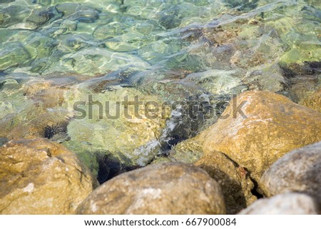 Adriatic sea water waves rolling on rocks at the beach.Crystal clear water with transparent surface shine under the bright summer sun at exotic tropical resort.Ocean tidal wave at seaside Royalty-Free Stock Photo #667900084