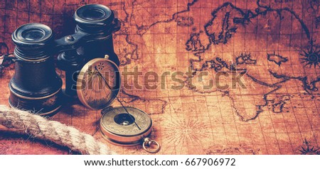 Old vintage retro compass and binoculars on ancient world map. Vintage still life. Travel geography navigation concept background. Toned image.
