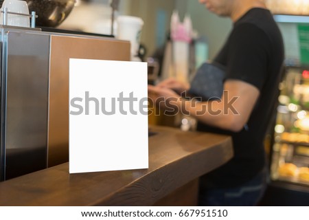 Mock up Menu frame on Table in Bar restaurant or coffee shop ,Stand for booklets with white sheets of paper acrylic tent card on cafeteria ,barista preparing cup of coffee for customer in background.