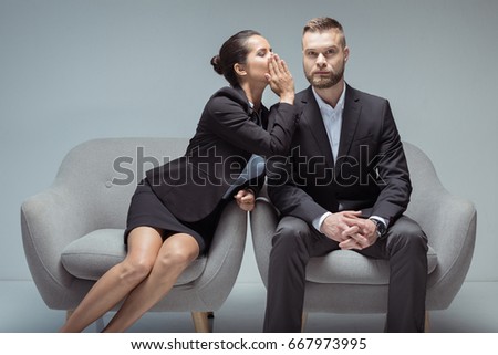 businesswoman whispering something on colleague's ear while sitting on chairs Royalty-Free Stock Photo #667973995
