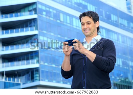 Business man playing in game on the phone. Man looking at smart phone against a blue building business center.