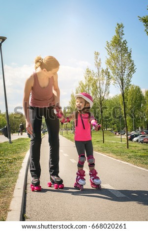 Mother and her little daughter inline skating on sidewalk. Mother and daughter enjoying in spring day.