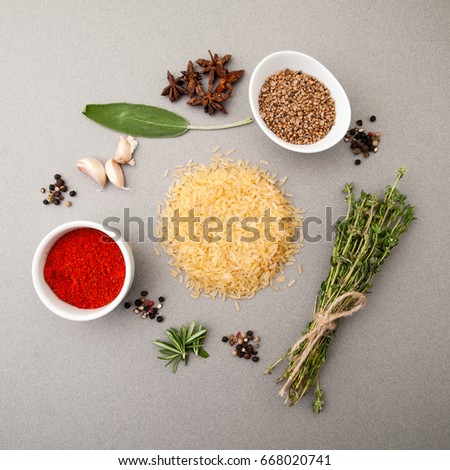 Rice groats, herbs and seasonings on a light gray stone table.
