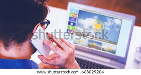 Digitally composite image of videos and computer icons against rear of man using mobile phone and laptop