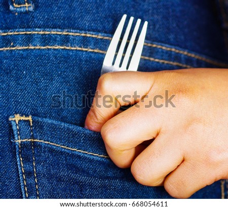 Woman hand holding a fork inside of jeans back pocket