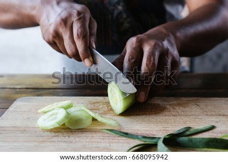 The chef's hand is cutting cucumber on a Chopping Wood in the kitchen