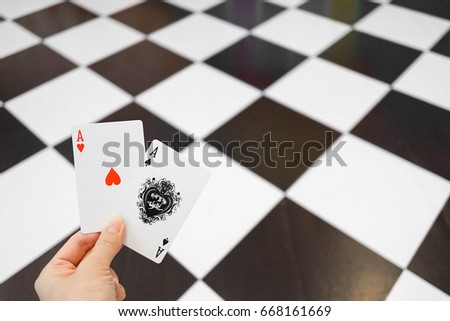 Hand holding Ace cards (red heart and black spade) over the abstract blur checkered floor background