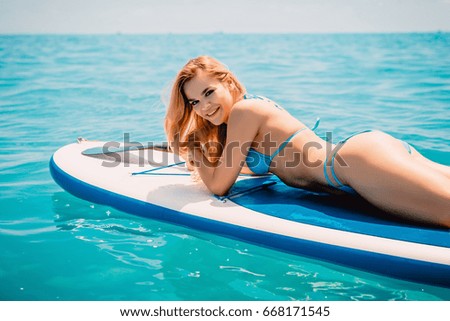 Blonde slim girl with perfect body in bikini relaxing on stand up paddle board on a sunny day