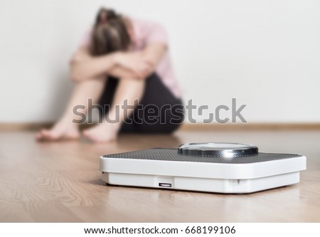 Weight loss fail concept. Scale and depressed, frustrated and sad woman sitting on floor holding head and arms on knees. Royalty-Free Stock Photo #668199106