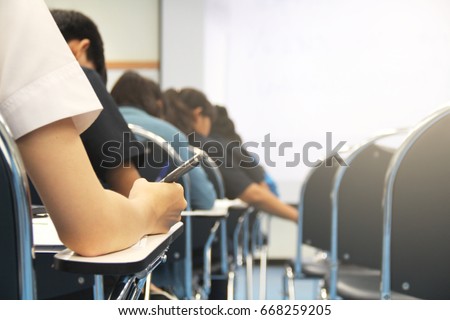 Hands university student holding pen writing /calculator doing examination / study or quiz, test from teacher or in large lecture room, students in uniform attending exam classroom educational school. Royalty-Free Stock Photo #668259205