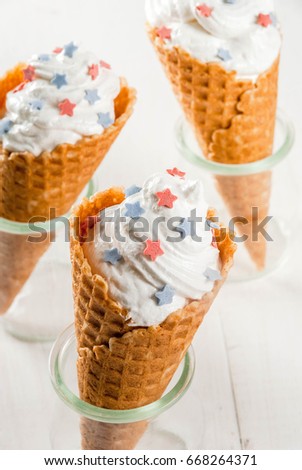 Treats for Independence Day holiday on July 4. Homemade cream ice cream in waffles, decorated with stars in traditional colors - blue, red, white. On a white wooden table, copy space