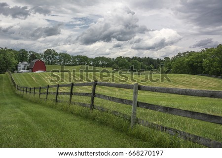 Landscape picture of a farm pasture enclosed by rustic fencing with a red barn.
