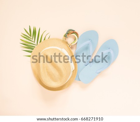 Summer fashion, summer outfit on cream background. Blue flip flops, seashell, wood bracelet and straw hat. Flat lay, top view