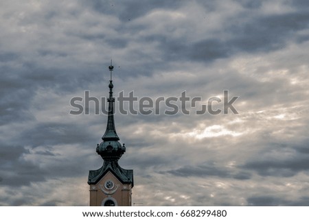 Spiky tower with a clock on a cloudy sky background