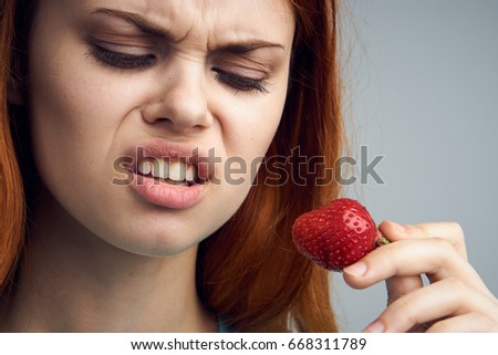 Emotion, portrait, young girl on a gray background holds a strawberry.
