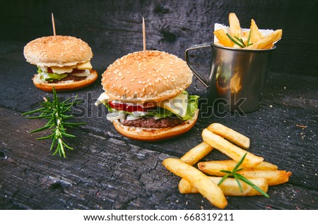 Hamburger with french fries on a burnt, black wooden table. Fast food meal. Homemade hamburger consist of beef meat, lettuce, tomato, bins, dressing, cheese and spices.  Vintage 