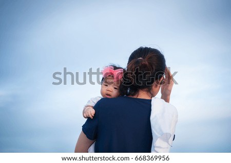 Mother day bonding concept with newborn baby nursing. Mother is holding newborn baby with flower pink headband with blue sky. Focus at infant girl