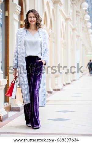 smiling beautiful middle aged woman in knitted bright summer coat with shopping bags in city shopping center