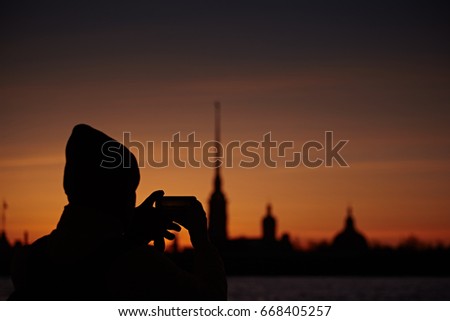 The tourist takes pictures on the smartphone St. Petersburg. Silhouette of the Peter and Paul Cathedral and man at sunset