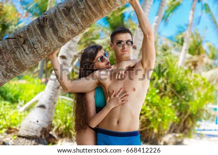 Young loving couple under a palm tree on a tropical beach. Tropical sky and sea in the background. Summer vacation concept.