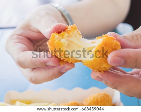 Hand is holding a stretch cheese ball ready to be eaten with soft focused french fries on blue table background Royalty-Free Stock Photo #668459044