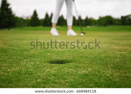 Green golf course with hole and blurred young woman on background