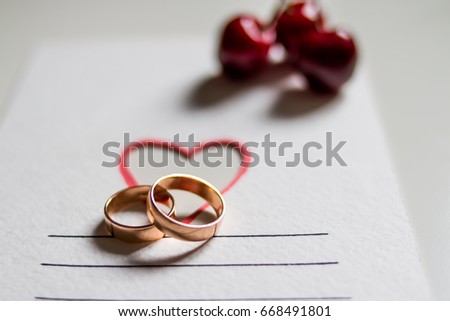 wedding rings and cherries on white postcard with heart. The concept of a wedding. Golden rings close up with cherry berries like background. Empty space for text. Invitation card.