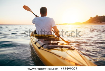 Rear view of kayaker man paddle kayak at sunset sea. Kayaking, canoeing, paddling Royalty-Free Stock Photo #668499073