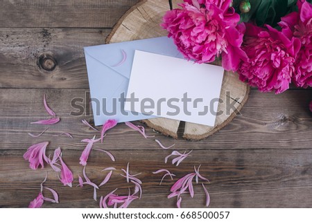 Row of peonies and paper card and on wooden background with space for message. Women's or Mother's Day background.
