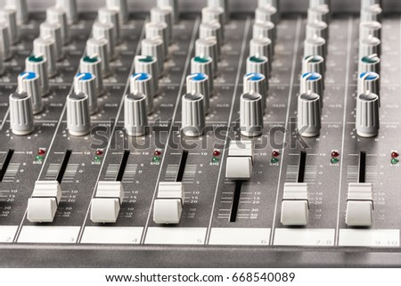Closeup macro audio mixing console knobs and sliders.