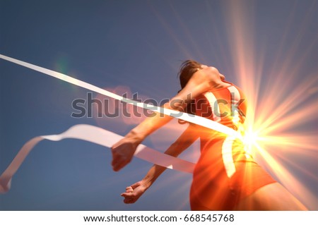 Low angle view of young female athlete crossing finish line against clear blue sky Royalty-Free Stock Photo #668545768
