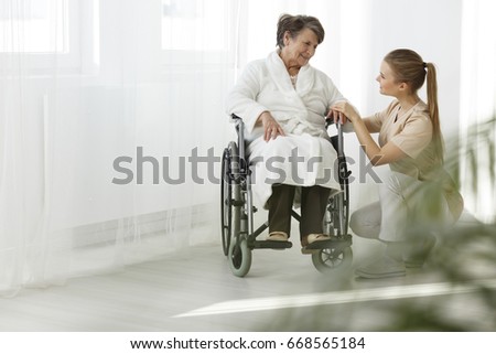 Senior lady in a wheelchair smiling at her nurse