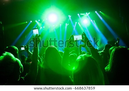 People in the crowd at a concert make video recordings and pics on a smartphone of published in social media