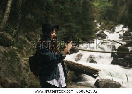 Hipster girl with backpack , tourist traveler taking pictures of amazing landscape on mobile sell phone digital camera on background valley view mockup