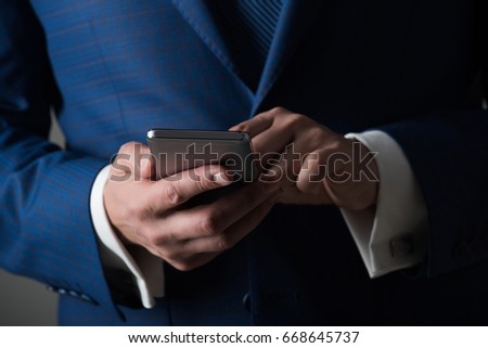 technology for business. Searching for information. Mobile phone or smartphone in male hands. Stylish blue formal jacket on grey background