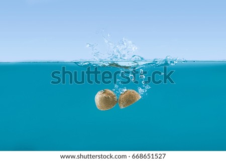 side view of fresh kiwi halves falling into water with splashes