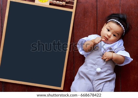 Asian healthy baby  lie leisurely on wooden floor near empty board.