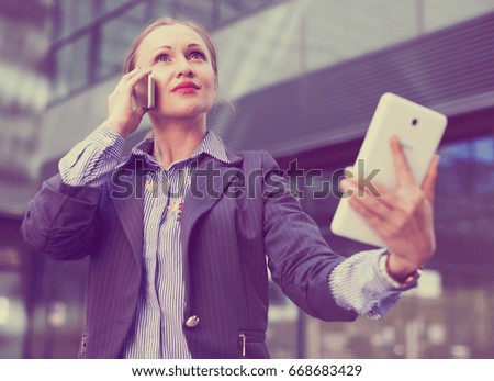 female testing digital tablet and talking on mobile phone in the modern city
