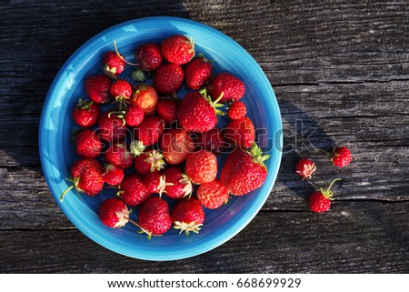 Juicy berries strawberry in a blue plate on a wooden old surface, close up, the top view