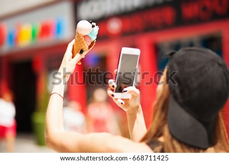 Pretty girl taking picture of ice cream on smartphone. Focus on ice cream