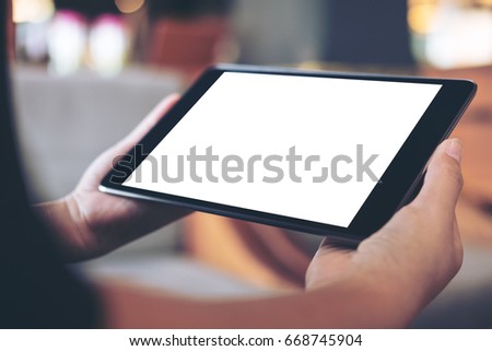 Mockup image of woman's hand holding black tablet pc with blank white screen in wooden cafe