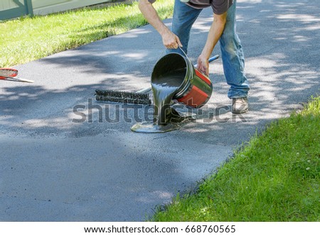 Do it yourself home maintenance. Driveway resealing repair. Homeowner pours blacktop sealant onto driveway Royalty-Free Stock Photo #668760565