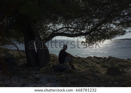 Man sitting under tree in shadow. Beautiful nature and landscape photo of warm summer evening in Croatia. Nice, calm and peaceful image.